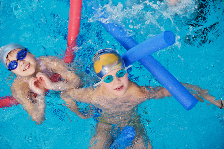 Image of 2 Kids in a swimming pool with swimming aids.
