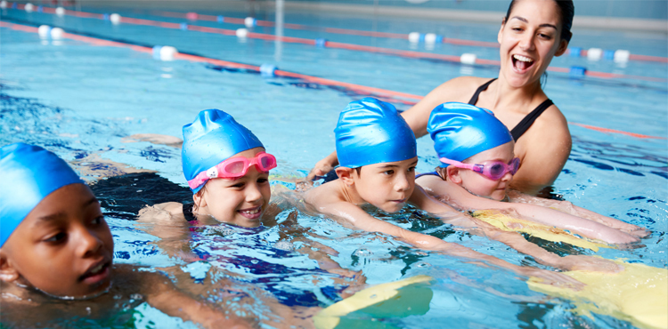 A picture of four young children learning to swim in a swimming pool with a swimming instructor