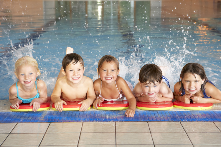 Image of 5 children kicking their legs in a swimming pool.